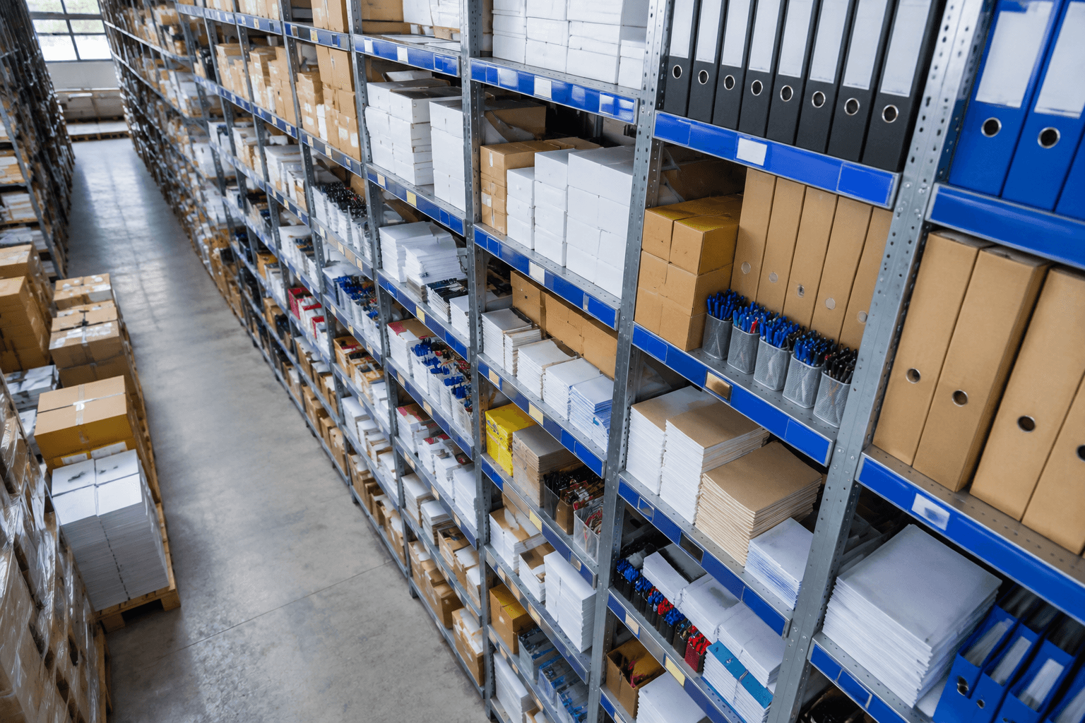Overhead view down a stockroom aisle of blue-labelled office stationery shelving